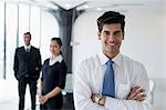 India, Smiling business man standing with arms crossed in front of colleagues