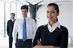 India, Smiling business woman standing with arms crossed in front of colleagues