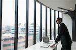 India, Businessman standing by desk and looking through window in office