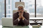 India, Portrait of senior businessman siting at desk with hands under chin