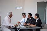 India, Three colleagues sitting at meeting table with senior businessman