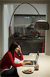 Singapore, Young woman using laptop in dining room at night