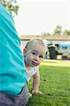 Baby boy peeping behind his mother in lawn, Munich, Bavaria, Germany