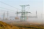 Electricity transmission lines are associated to  autumn landscape. Industrial constructions are shrouded in morning mist.