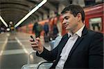 Young businessman using smartphone while waiting at the underground station. Blurred platform, train and people in background