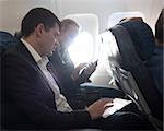 Young businessman working with digital tablet and woman using smart phone during the flight. Bright sunlight in plane window