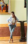indoor fashion portrait of young brunette female wearing torn jeans, heels and jacket. Posing in old palace with canvas backward