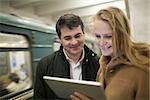 Happy young couple watching something on tablet computer in underground. Train passing by