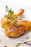 Closeup shot of baked chicken leg with thyme on white baking paper.