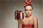 lovely sexy woman with freckles and creative golden glitter christmas make-up taking gift box in the hand. Red decorated ribbon on hair-style and on breast.