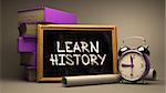 Learn History. Motivational Quote Handwritten by white Chalk on a Blackboard. Composition with Small Chalkboard and Stack of Books, Alarm Clock and Rolls of Paper on Blurred Background. Toned Image.