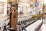 young woman standing near town bicycle , in winter time . she is wearing a brown coat. looking down