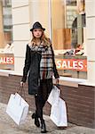 beautiful girl walking near a window shop , in the street . she is doing shopping in winter sale , dressing a coat and hat