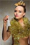 sexy girl with freckles posing in creative christmas portrait with golden ribbon in the hair-style, christmas glossy make-up and shiny tinsel around neck. Taking little bell in the hand