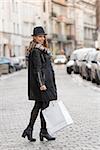 elegant and cute woman , in the middle of a road , with shopping bag for winter sale , she is wearing voat and a nice hat