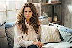 Half length portrait of elegant woman with long brown hairs sitting on sofa in loft living room