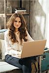 Portrait of elegant dressed brunet woman sitting in loft apartment and working on portable laptop