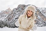 Magical mix of winter season and mountain landscape create the perfect mood. Portrait of cheerful young woman in white coat and fur hat outdoors