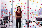 Mixed race woman working in modern office with reminders on skyscraper window. The girl feels stressed, holds a sticking note with sad emoticon on mouth.