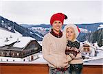 Mountain cottage hideaway brings calm and warmth into the winter season. Portrait of happy mother and child in Santa hat standing on balcony overlooking the snow-capped mountains