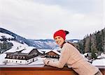 Mountain cottage hideaway brings calm and warmth into the winter season. Portrait of smiling young woman standing on balcony overlooking the snow-capped mountains