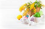 Easter eggs with white rabbits and branch mimosa on wooden board. Isolated on white background