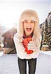 Christmas season in relaxed style of contemporary countryside living. Cheerful young woman in white sweater holding red cup in the front of a cosy mountain house.