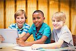 Cute pupils using tablet computer in library against window overlooking city