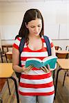 Student reading book in library against empty classroom