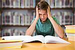 Student sitting in library reading  against books on desk in library