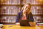 Student studying in the library with tablet against books on desk in library