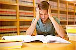 Student sitting in library reading  against close up of a bookshelf