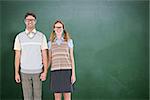 Smiling geeky hipster couple holding hands  against green chalkboard