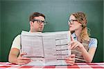Geeky hipster couple reading newspaper against green chalkboard