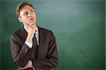 Young businessman thinking with hand on chin against green chalkboard