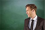 Young handsome businessman looking away against green chalkboard