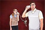 Geeky hipster couple speaking with tin can phone  against desk
