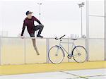 Urban cyclist climbing over fence on sports field