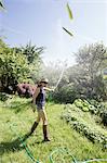 Side view of mature woman in garden squirting water into air with hosepipe