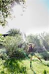 Front view of mature woman in garden standing on one leg squirting water into air with hosepipe