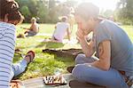 Young adults playing board game at sunset party in park