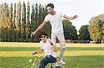 Two male friends fooling around on bicycle in park