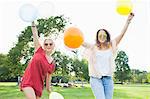 Portrait of two young women dancing with balloons at park party