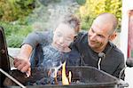 Mid adult man and son lighting barbecue in garden