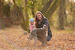 Mid adult woman and baby daughter petting dog in autumn park