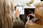 Mother and daughter sitting together in cafe, looking at digital tablet, rear view