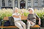Mother and daughter sitting on bench, daughter taking photograph of mother using smartphone