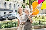 Mother and daughter walking along street together, holding bunch of balloons