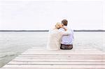 Mature couple sitting on pier, looking at view, rear view