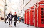 Young shopping couple strolling past red phone boxes, London, UK